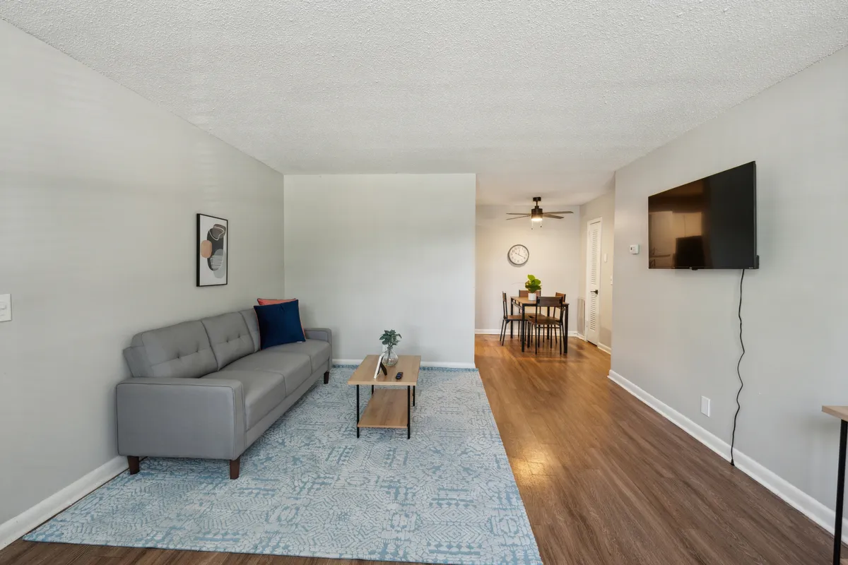A comfortable living room setup with a sofa, coffee table, modern artwork, and a dining area visible in the background. The layout encourages both entertaining and casual gatherings, with decor that feels contemporary and welcoming.