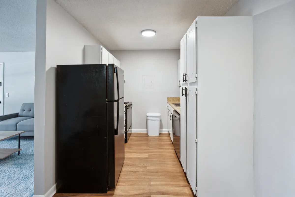 A modern kitchen scene featuring a striking black refrigerator paired with pristine white cabinets and a warm wooden countertop. The layout is open and user-friendly, inviting culinary creativity and social interaction. Subtle decorative elements add personality and a lived-in charm.