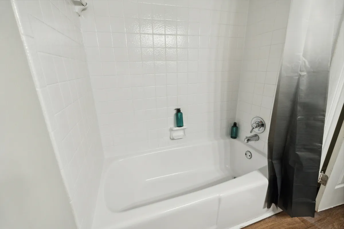 A calming bathroom scene featuring a sleek bathtub with a showerhead, soap dispenser, and a bottle of shampoo. The ambiance is fresh and soothing, ideal for self-care routines and relaxation after a busy day.