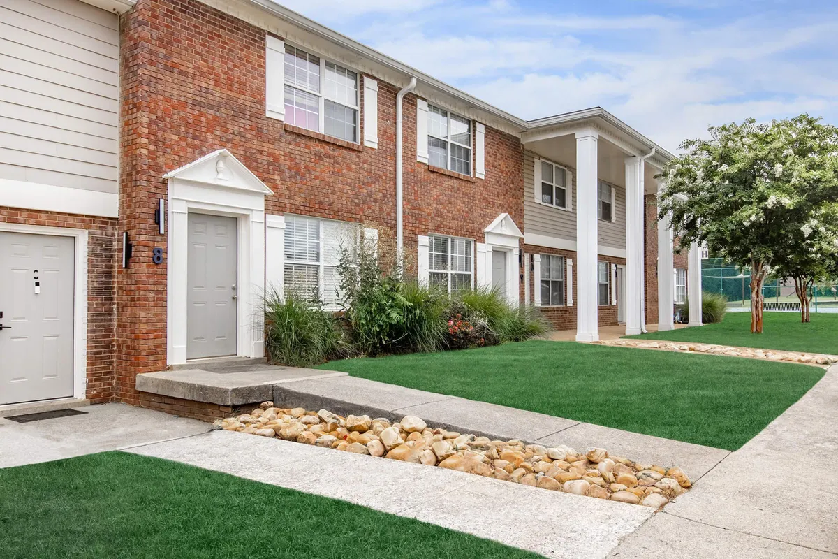 A warm, welcoming brick facade with a landscaped garden and a clear pathway leading to the front door. The outdoor setting suggests a sense of arrival and the comfort of returning home after a day out.