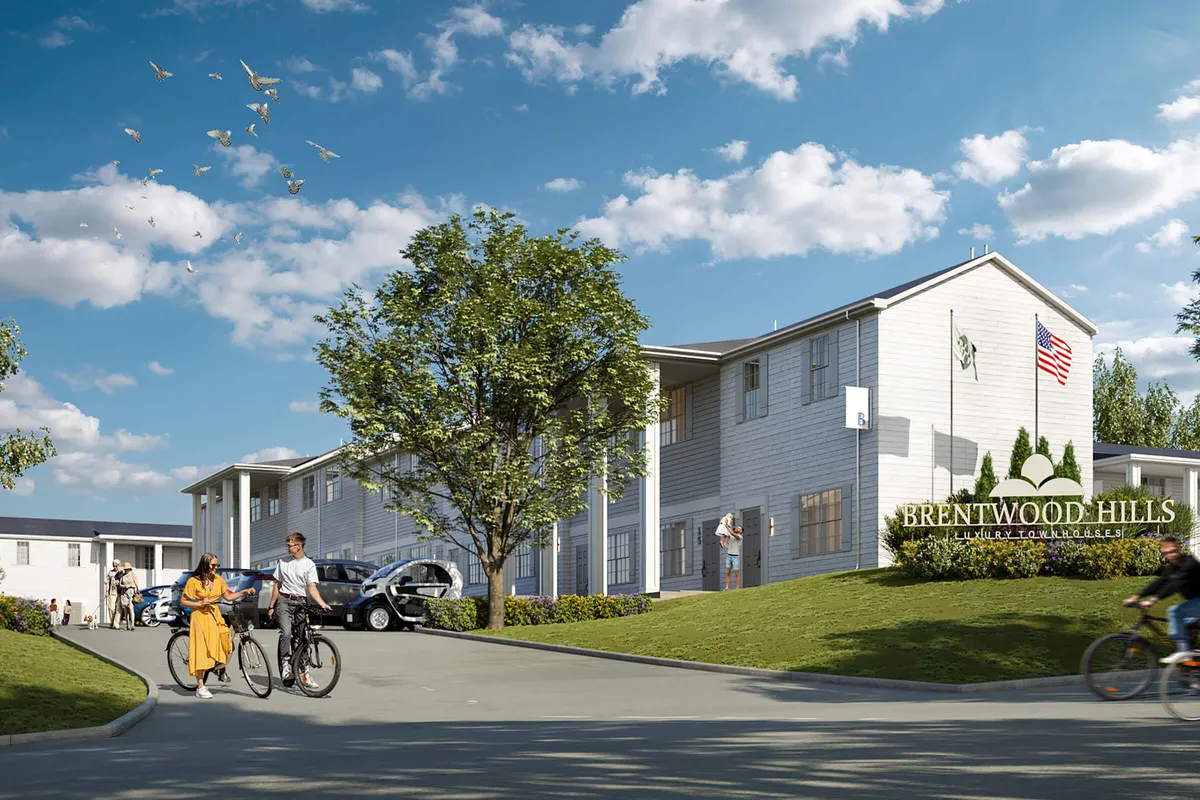 A modern townhome complex with well-maintained greenery and an American flag, featuring scenic walking and biking paths. The inviting courtyard hints at a lively and active community atmosphere perfect for launching urban adventures.