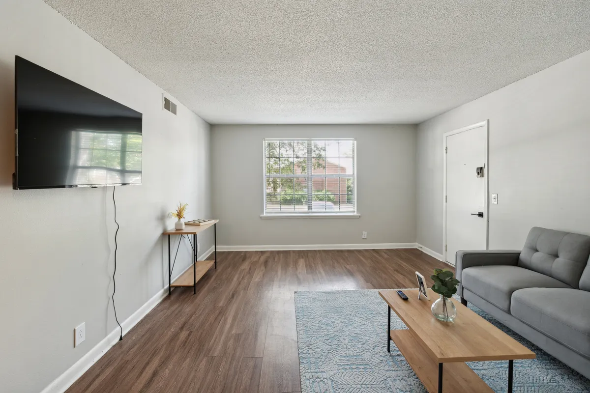 A cozy living space with a soft sofa, coffee table, wall-mounted television, and a large window bringing in sunlight. The room is arranged for comfort and socialization, ideal for movie nights or morning relaxation.