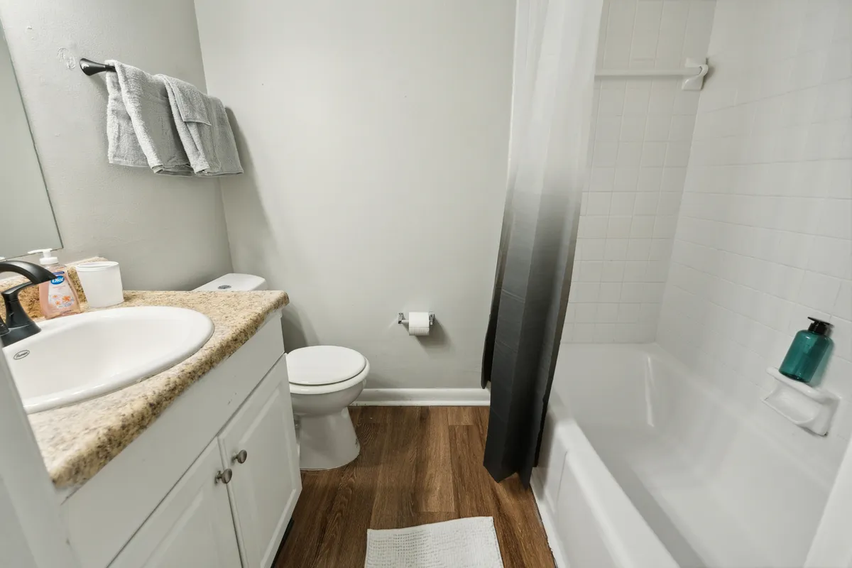 A modern, clean bathroom with a granite countertop sink, toilet, and a shower-tub combo. Towels hang neatly on the wall, and the space is organized and inviting—ideal for both quick freshen-ups and relaxing routines.